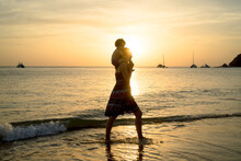 Thailand, Koh Lanta, Silhouette Of Mother With Baby Girl On Her Shoulders At Seashore During Sunset
