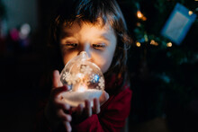Little Girl Holding Lighted Glass Ball At Christmas Time