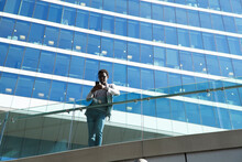 Male Professional Using Smart Phone While Standing By Glass Railing Against Office Building