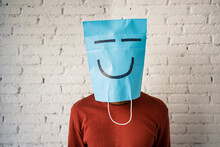 Mid Adult Man Wearing Blue Paper Bag On Face Against White Brick Wall