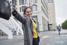 Cheerful Businesswoman Holding Laptop Bag While Standing With Arms Raised In City
