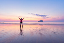Mature Woman With Arms Raised Standing At Seacliff Beach During Sunset, North Berwick, Scotland