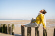 © Uwe Umst√§tter/Westend61 - Mature woman with eyes closed sitting on wooden post at beach against clear sky