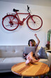 © victor espadas/Westend61 - Happy woman using laptop in living room at home with vintage bicycle hanging on the wall