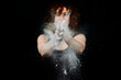© victor espadas gonzalez/Westend61 - Woman clapping hands covered with white dust in front of face against black background