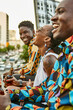 © victor espadas/Westend61 - Laughing friends sitting on roof terrace in the city drinking beer, Maputo, Mozambique