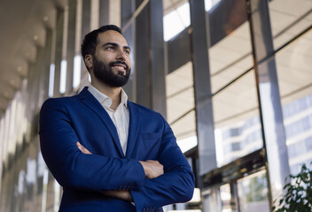 Wall Mural - Portrait of handsome middle eastern businessman looking away standing in office, copy space. Young pensive entrepreneur brainstorming,  planning start up project. Successful business