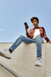 © victor espadas gonzalez/Westend61 - Young woman using smart phone while sitting on retaining wall against blue sky
