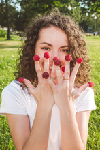Playful Young Woman With Raspberries On Fingers At Park During Sunny Day