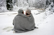 © Vasily Pindyurin/Westend61 - Young couple covered in blanket looking at each other while sitting by frozen river in forest