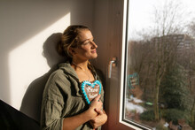Smiling Young Woman At The Window Holding Gingerbread Heart