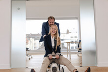 Playful Businessman Pushing Businesswoman On Toy Car In Office