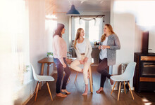 Mother And Daughters Standing In Kitchen, Talking, Drinking Coffee