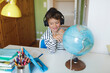 © Hannes_Eichinger/Westend61 - Boy doing homeschooling with a globe and using tablet and headphones at home