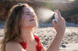 © IVAN GENER/Westend61 - Young woman applying suncream spray on the beach