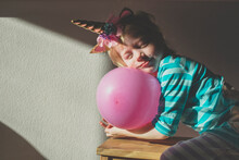 Portrait Of Little Girl With Eyes Closed Wearing Unicorn Horn Leaning On Pink Balloon