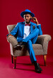© Alvaro Gonzalez/Westend61 - Confident man wearing blue suit sitting on chair against red background