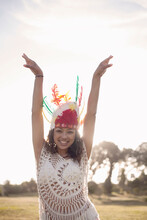 Happy Woman Wearing Native American Headdress Standing With Hand Raised At Park