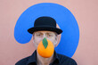 © Petra Stockhausen/Westend61 - Portrait of man with an orange at a wall with question mark wearing a bowler hat