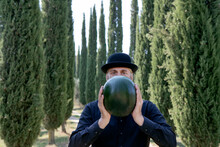 Italy, Tuscany, Man Surrounded By Cypresses Wearing A Bowler Hat Holding A Melon