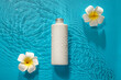 Bottle of cosmetic product and plumeria flowers in water on color background
