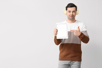 Wall Mural - Young man with tablet computer and headphones on light background