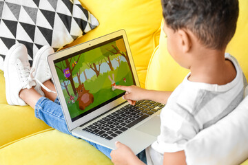 Sticker - Little African-American boy pointing at laptop while watching cartoons on sofa at home