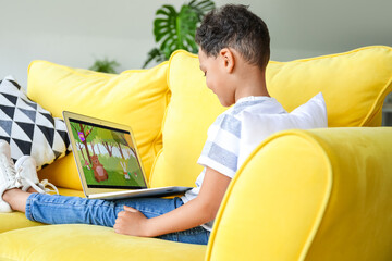 Sticker - Little African-American boy with laptop watching cartoons on sofa at home