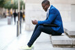 © Lifestock/Westend61 - Young businessman wearing blue suit jacket, sitting on step and using smartphone