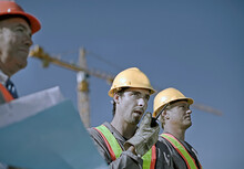 Male Construction Worker Talking On Walkie-talkie By Coworkers At Construction Site Against Clear Sky