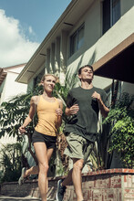 Young Man And Woman Running Together Along Street On Sunny Day