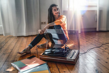 Young Woman Sitting On The Floor At Home With A Record Player