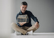 © KNSY/Westend61 - Confident mature businessman sitting on the floor holding glass house model