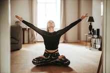 Woman Sitting In Lotus Pose With Raised Arms At Home