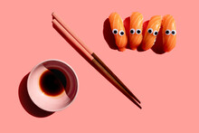 Studio Shot Of Chopsticks, Bowl Of Soy Sauce And Salmon Nigirizushi Pieces With Googly Eyes