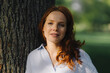 © Kniel Synnatzschke/Westend61 - Portrait of redheaded woman at tree in a park