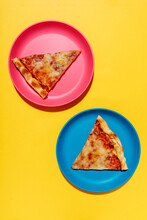 Two Slices Of Pizza Margherita On Blue And Pink Plates Against Yellow Background