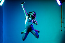 Cheerful Girl Jumping While Listening Music Against Blue Wall In Studio