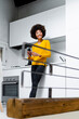 © Westend61 - Portrait of smiling young woman standing in the kitchen with smartphone
