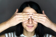 © Giorgio Fochesato/Westend61 - Smiling young woman covering eyes with hands against gray background
