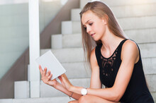 Portrait Of Young Woman Sitting On Stairs Using Mini Tablet