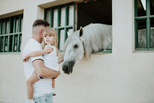 Father Carrying Cute Daughter While Stroking Horse At Stable