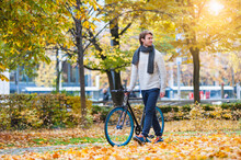 Young Man Pushing His Bicycle In Autumnal Park