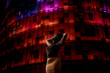 © Gala Mart√≠nez L√≥pez/Westend61 - Woman with arms raised standing against red illuminated building in city