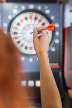 Close-up Of Woman's Hand Holding Dart In Front Of Dartboard