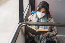 Woman Wearing Protective Mask While Reading Book In Bus