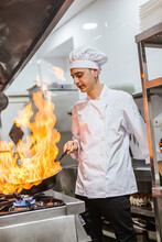 Junior Chef With Pan Of Flames In Traditional Spanish Restaurant Kitchen