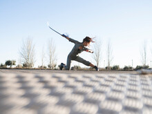 Young Woman With Sword Practicing Martial Arts In Park Against Clear Sky