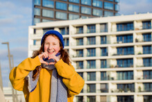 Smiling Girl Showing Heart Shaped Gesture While Standing Against Building