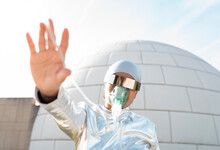 Young Woman In Protective Suit With Oxygen Face Mask And Futuristic Sunglasses Showing Stop Gesture While Standing Against Igloo